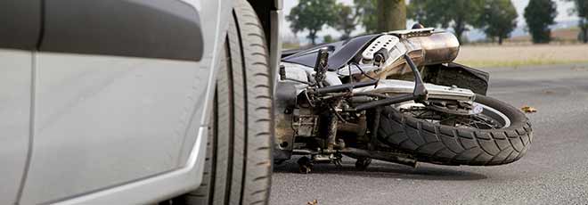 A motorcycle on its side in front of a silver car after being in an accident.