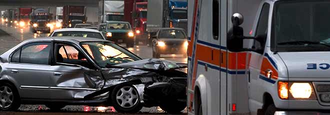 An ambulance sitting in front of a severely damaged vehicle after a car accident.