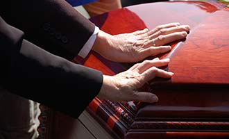 Hands touching a casket during a funeral.
