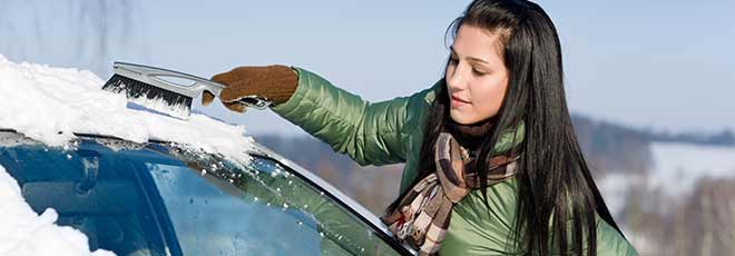 woman brushing snow off car in cold weather