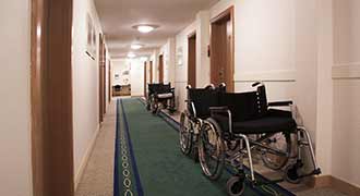An empty hallway in a nursing home with a row of empty wheelchairs.