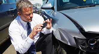 man taking pictures of damage to car after a Rhode Island auto accident