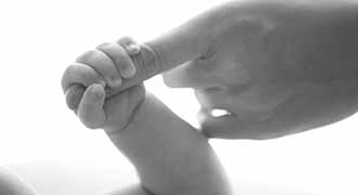 A newborn holding the finger of their parent.