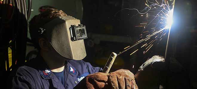 A welder using his tools to weld metal.