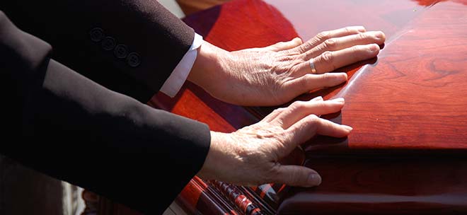 Hands touching a casket during a funeral.