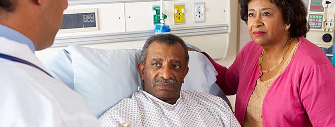 A man in a hospital bed with his wife next to him. They are talking to his doctor.