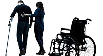 An aid is assisting someone to walk after they get out of a wheelchair.
