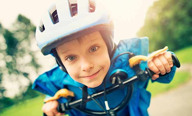 A little kid with a helmet on riding his bike.