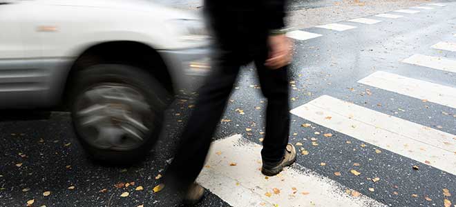 A SUV about to hit a pedestrian in a crosswalk.