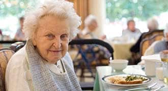 An elderly woman eating at a dinner table. 