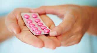 A person holding a pack of pink pills. 