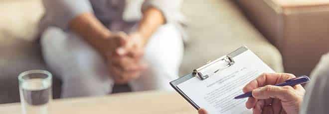 A psychiatrist is taking notes from a patient sitting across from them. 