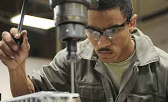 A worker uses a drill press at work.