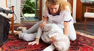 A nursing home employee helping an elderly lady off the floor.