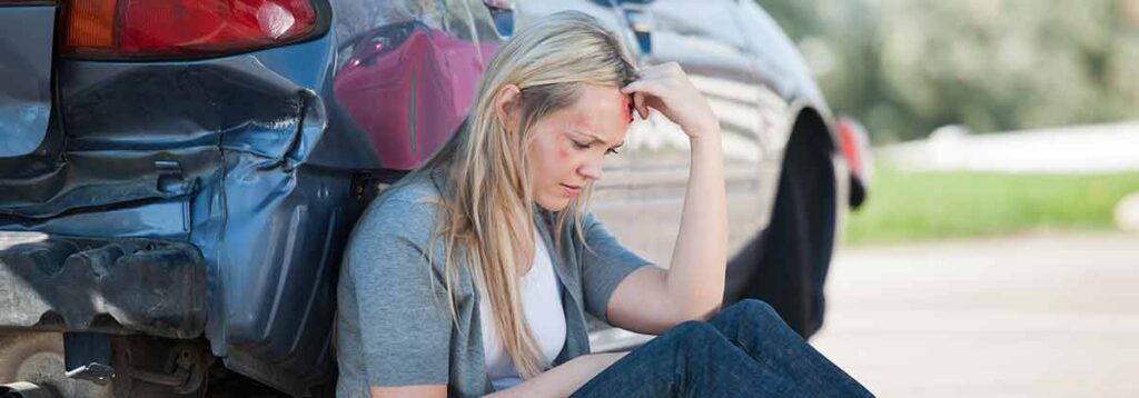 Woman sitting next to damaged car after an auto accident