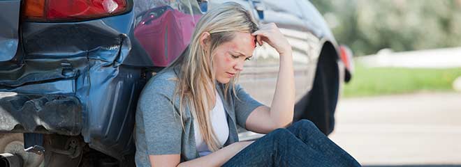 Woman sitting on ground after car accident
