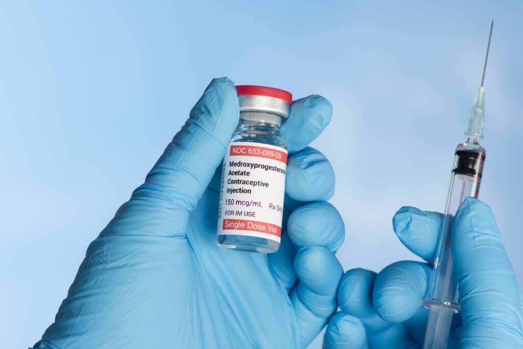 injection vial held in nurse's gloved hand with syringe.